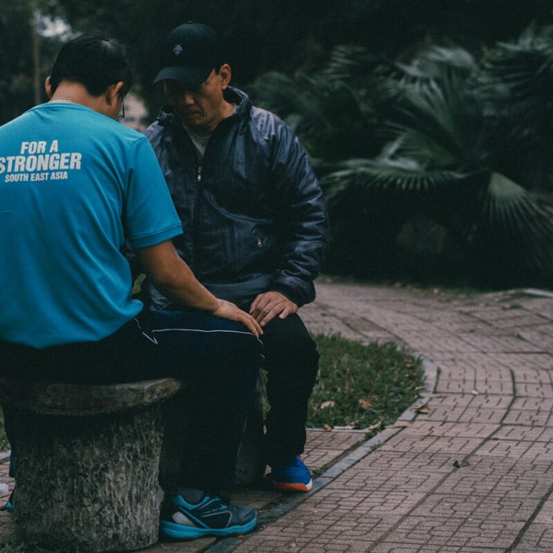 Two men sit on a stone bench outside.